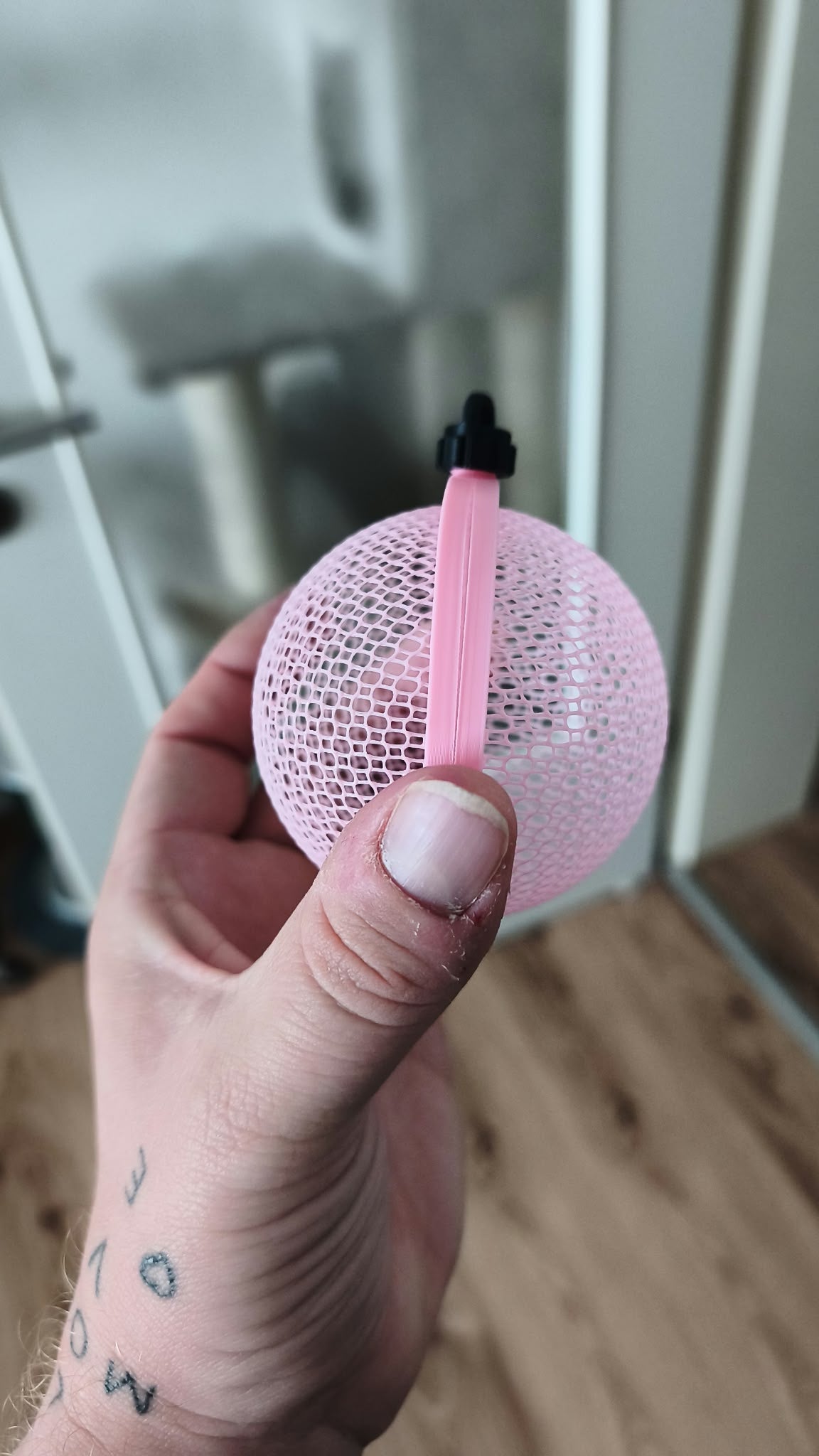 Seitenansicht: Seitenansicht der rosa Weihnachtskugel mit umlaufendem Mittelsteg, offener Gitterstruktur und schwarzem Aufhänger.