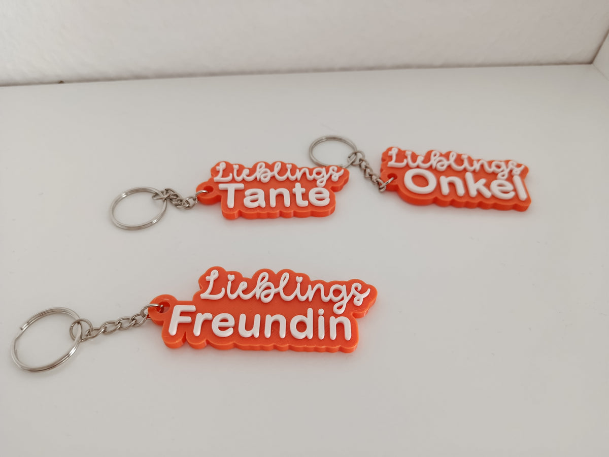 Drei 3D-gedruckte Schlüsselanhänger mit den Aufschriften Lieblings Tante, Lieblings Onkel und Lieblings Freundin