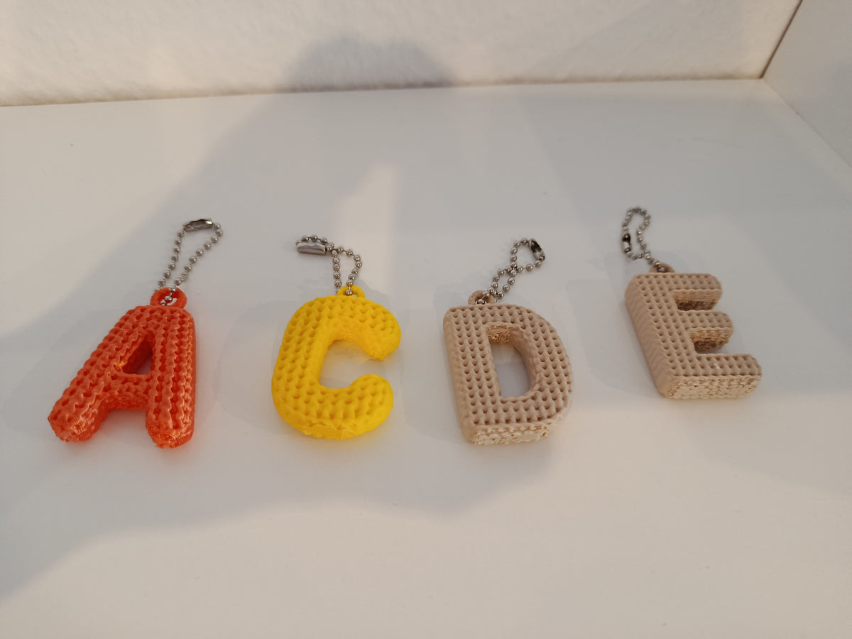 Personalisierte Schlüsselanhänger mit den Buchstaben A, C, D und E in Strickoptik