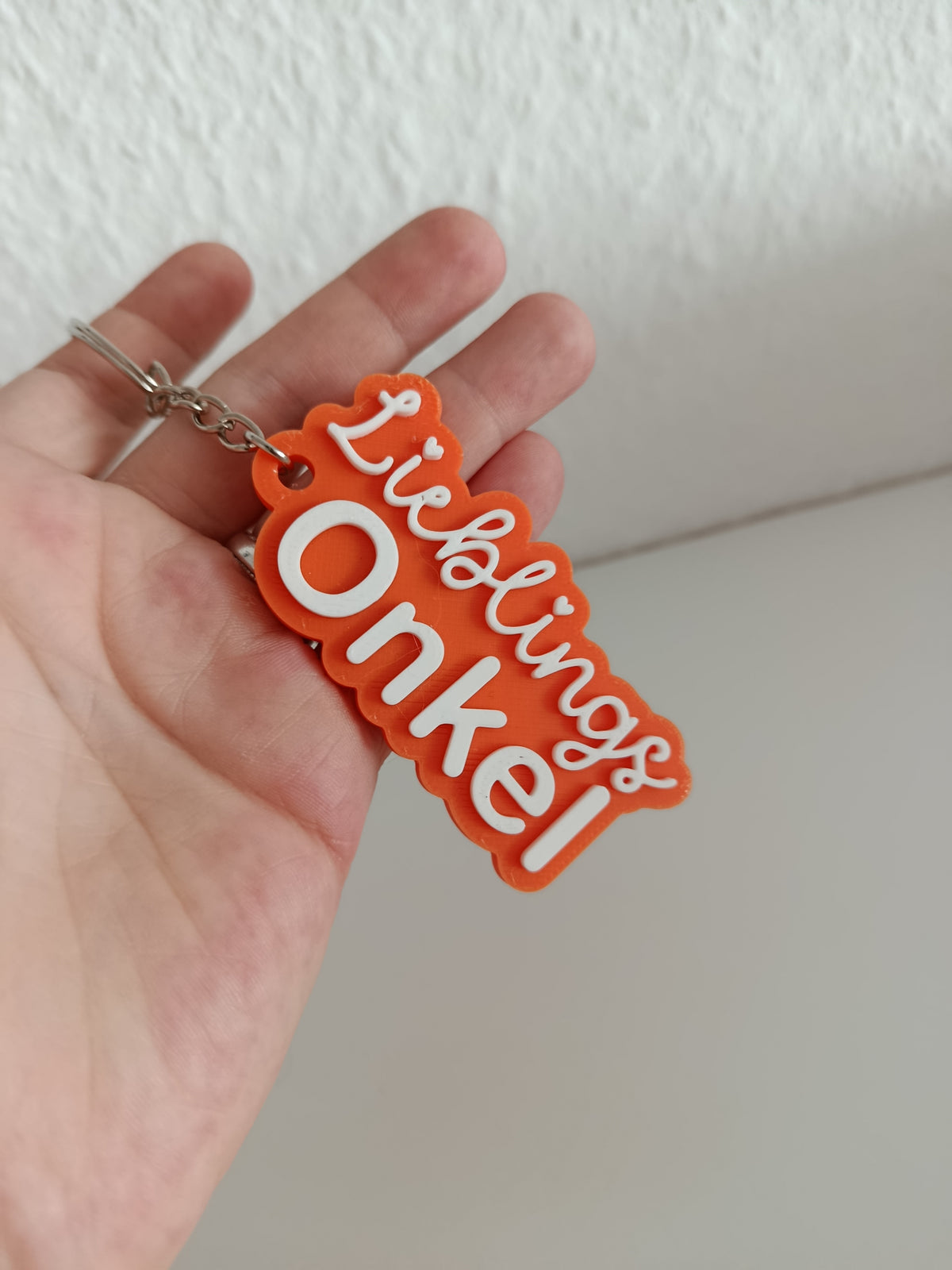 3D-gedruckter Schlüsselanhänger Lieblings Onkel in einer Hand gehalten, orange mit weißer Schrift