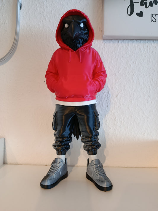 Schwarze Raben-Figur im roten Hoodie, schwarzer Hose und grauen Sneakers